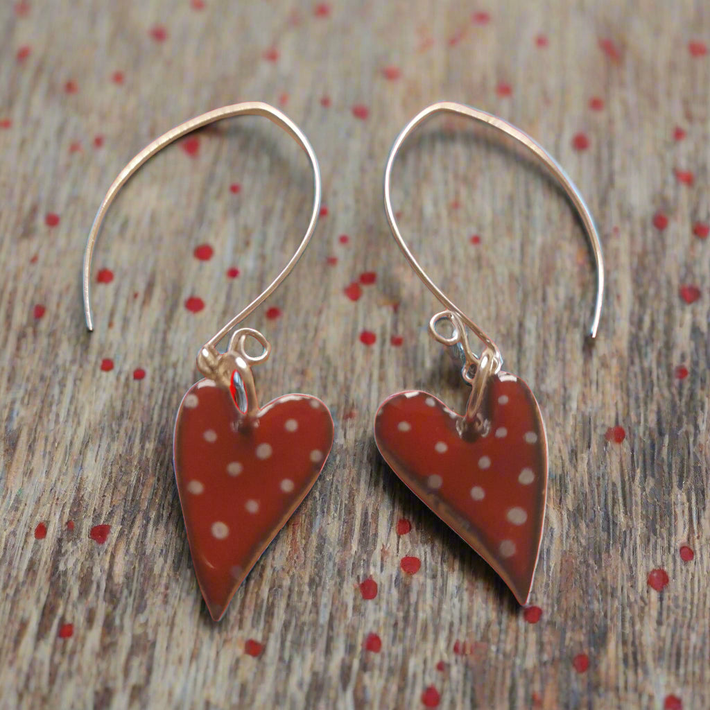 Quirky red heart earrings with polka dot design, presented on handmade silver earwires. On a wood background with red spots. 