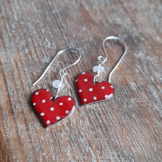 Red heart polka dot earrings, handpainted with handmade silver erwires and a small white bead between earring and earwire, on a grainy wood background 