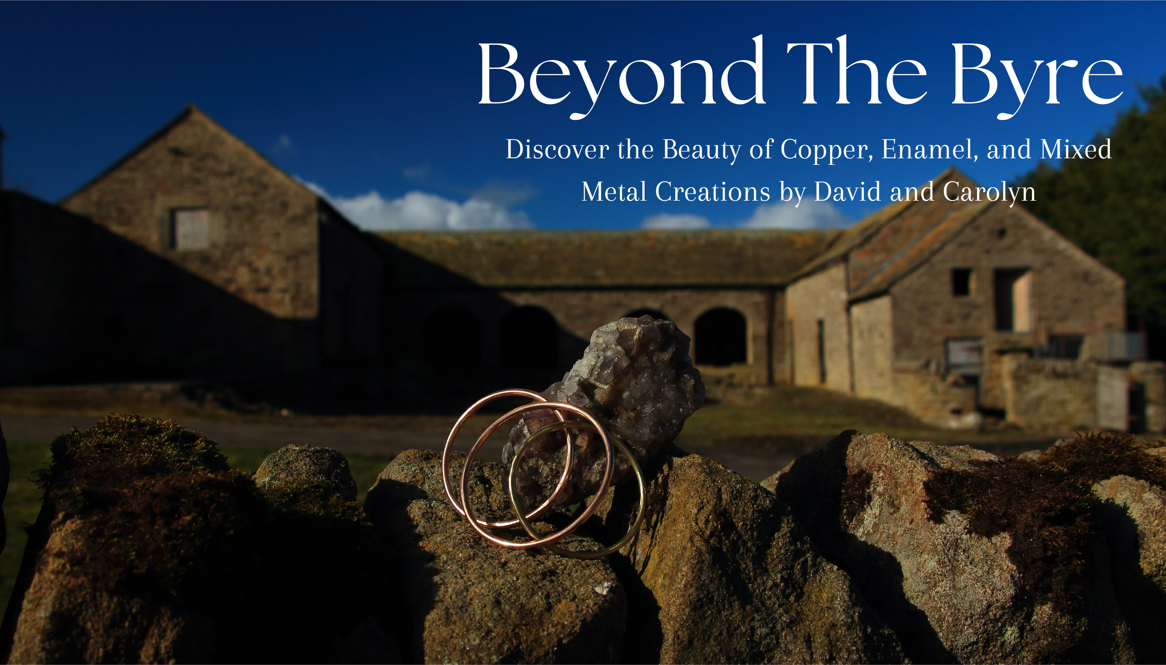 3 copper and brass handmade round bangles in sunlight on a stone wall overlooking the building Beyond The Byre Jewellery is named after. Discover the beauty of copper, enamel and mixed metal creations by Carolyn and David