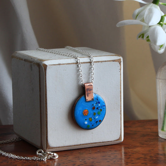 Teal, turquoise blue round enamel pendant on sterlig silver fine 18 inch fine trace chain. Colourful flecks decorate the right hand side of the pendant and the copper bail is integral to the pendant. The clasp and jump rings are sterling silver and soldered for extra security.